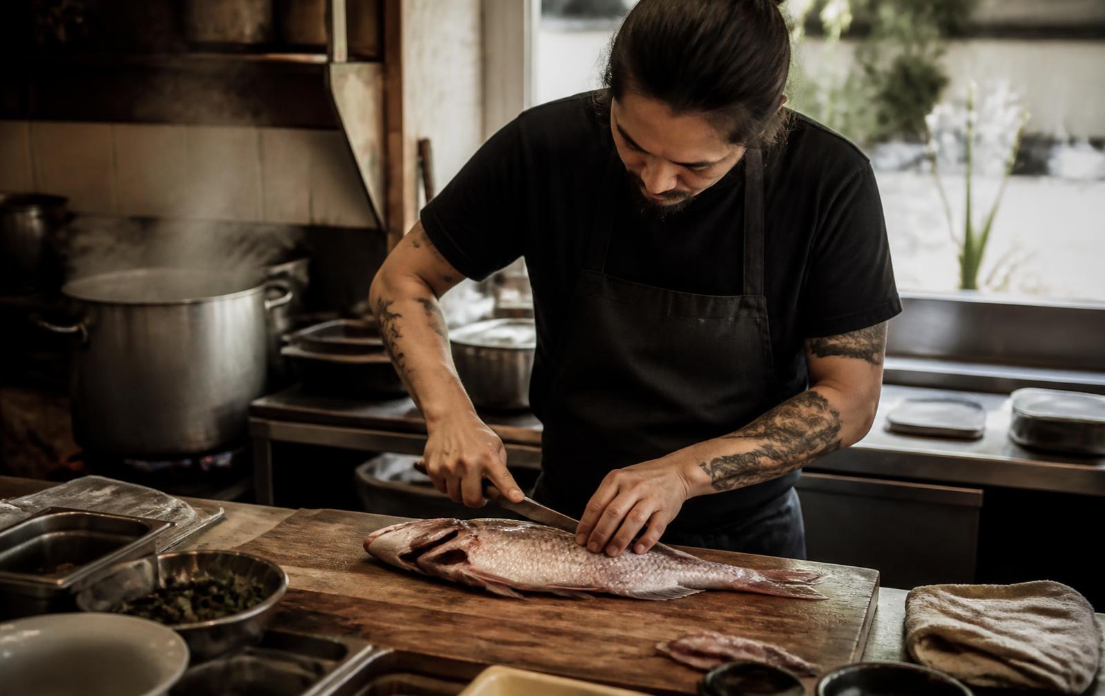 A cook breaking down a whole fish on a wooden board